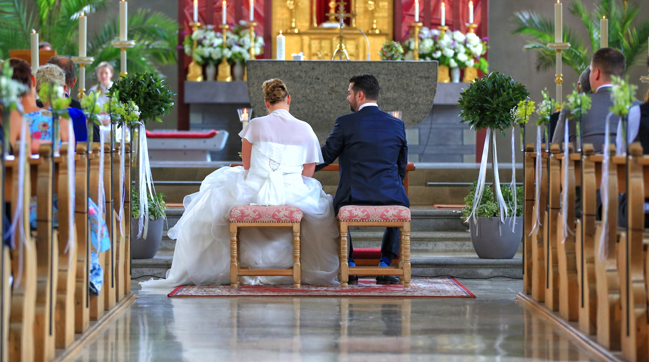  Sitzendes Brautpaar in der mit Blumen beschmückten Kirche von hinten - das Bild wird mit Klick vergrößert 