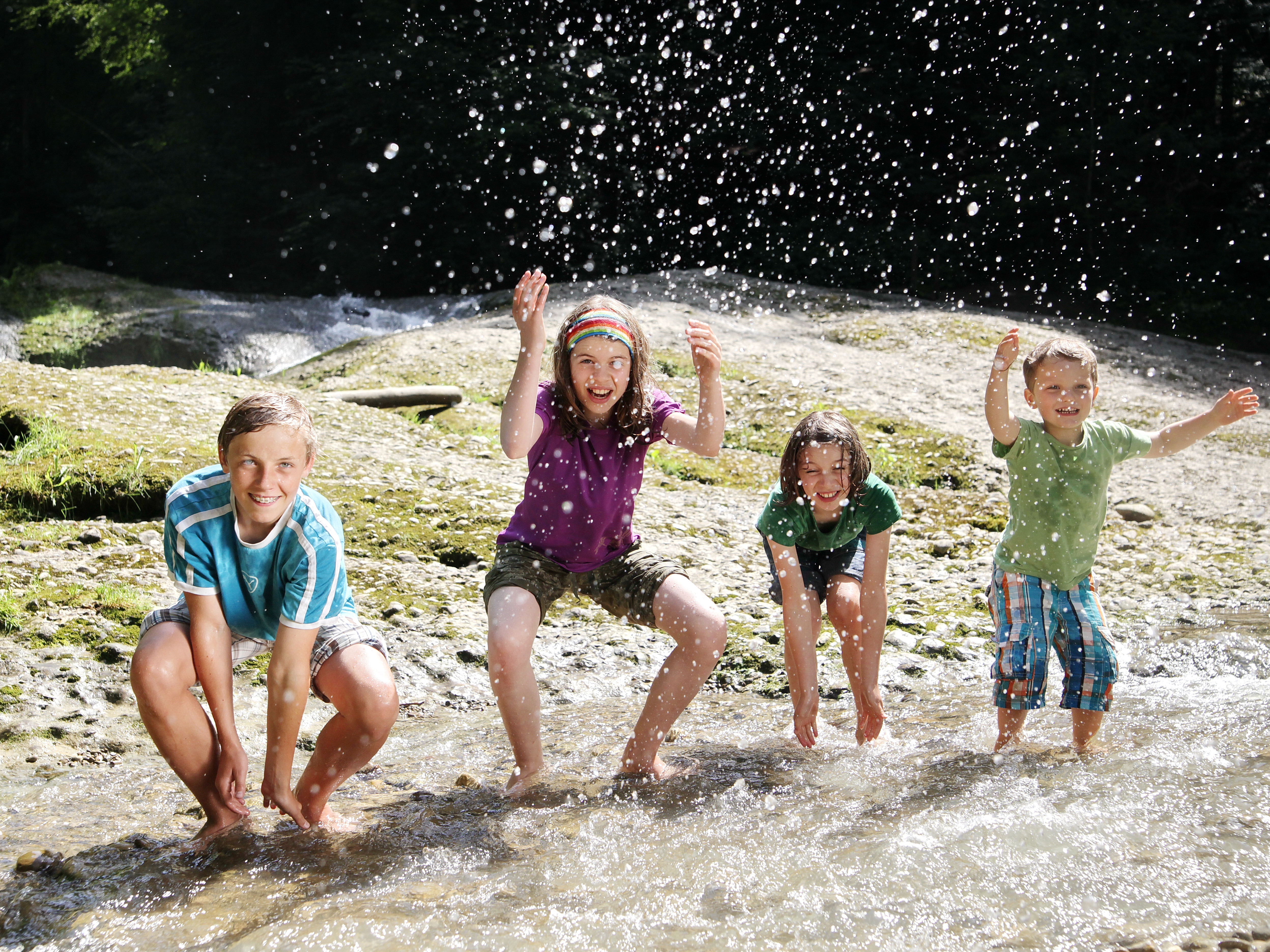  Vier Kinder spielen am Wasser und spritzen es hoch - das Bild wird mit Klick vergrößert 